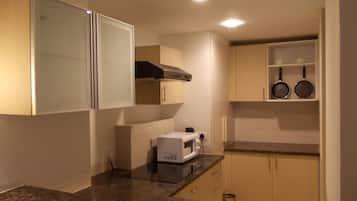 A compact kitchen with a microwave, stove, and two frying pans on a shelf.