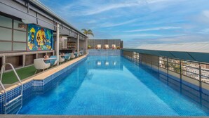 A rooftop infinity pool with a clear view of the city skyline, a bar area with seating, and a mural on the building facade. - Radisson Hyderabad Hitec City (Hyderabad)