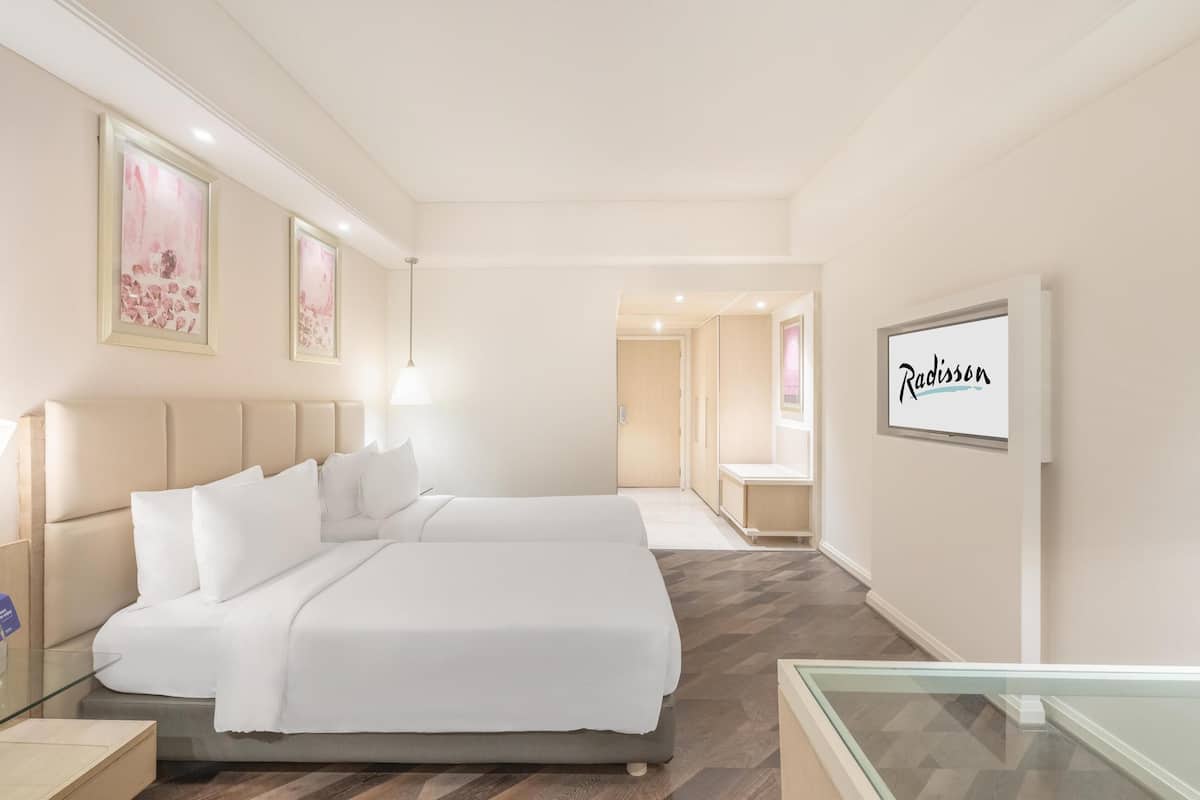 A hotel room with a large bed, a bedside table, a nightstand, a glass partition, and a framed sign on the wall.