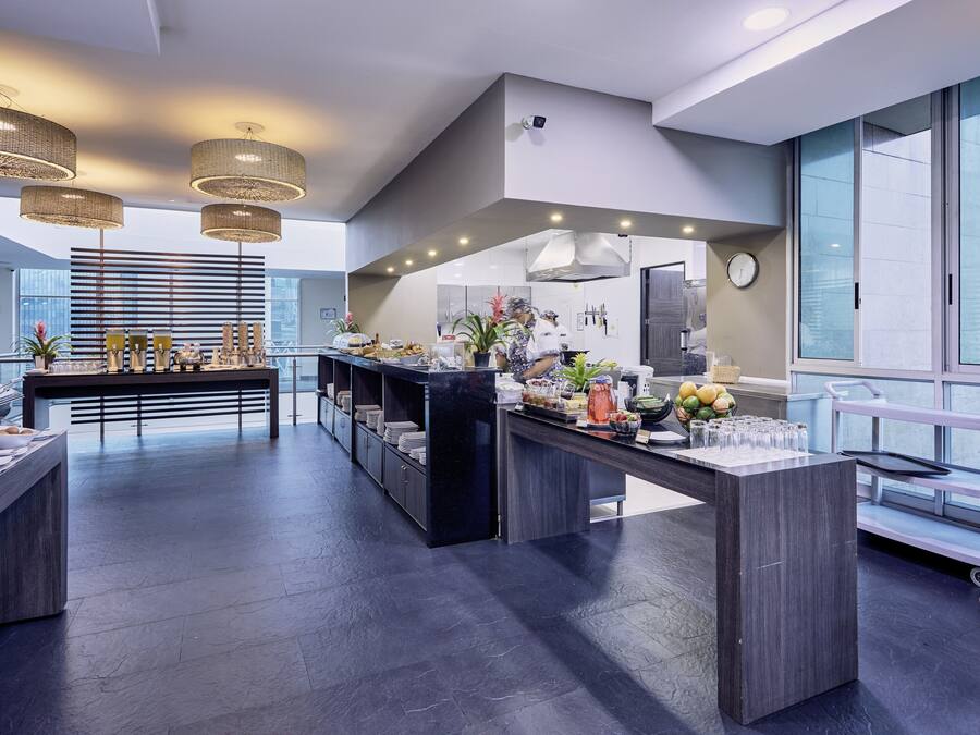 A modern kitchen with a central island, a buffet setup, and a view of the city through large windows.