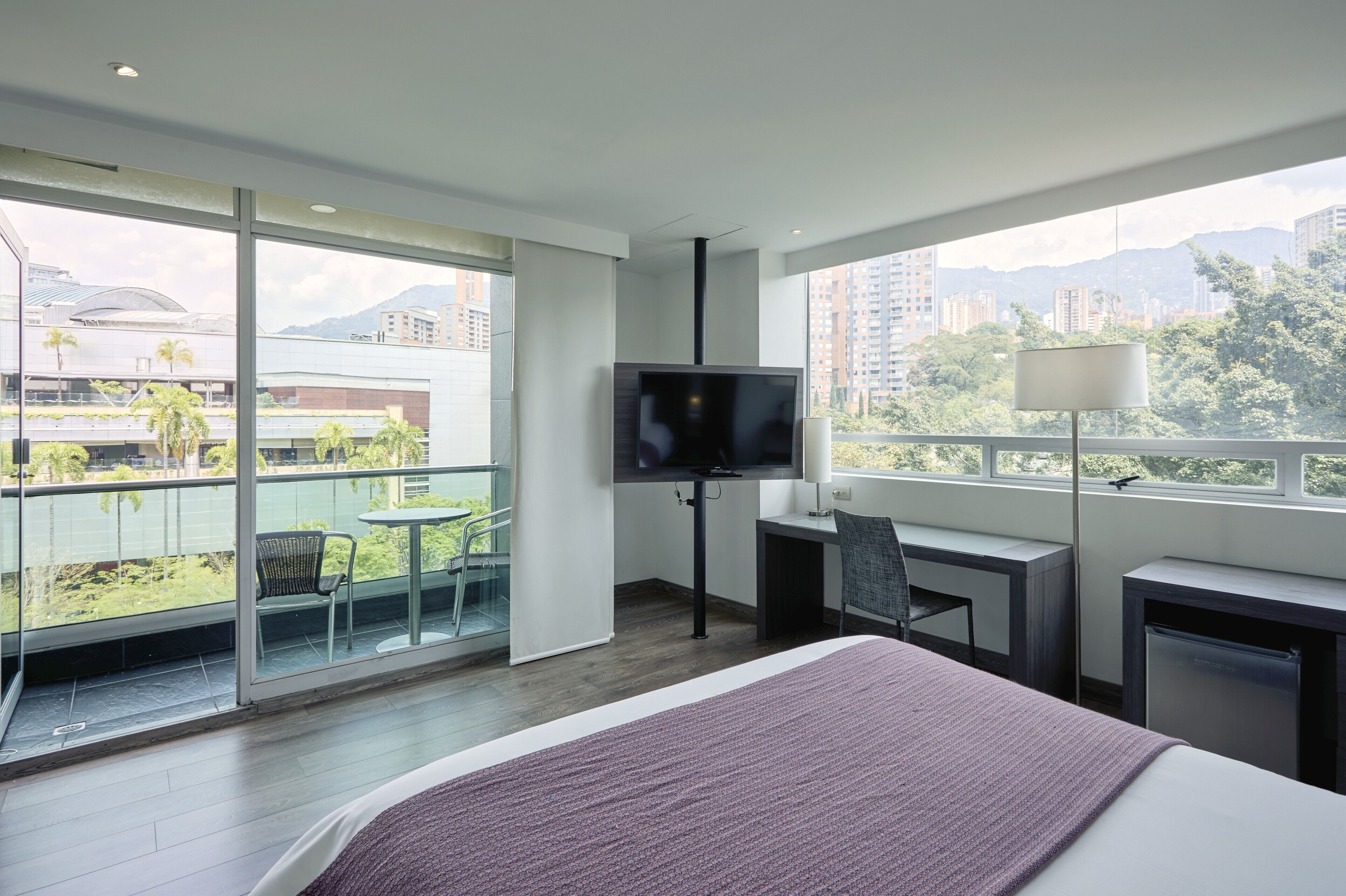 Habitació d'hotel amb un llit, escriptori, televisió i un balcó amb vista a la ciutat.