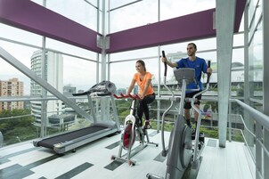 Un gimnasio con dos personas usando bicicletas estáticas, una caminadora y una máquina de remo.