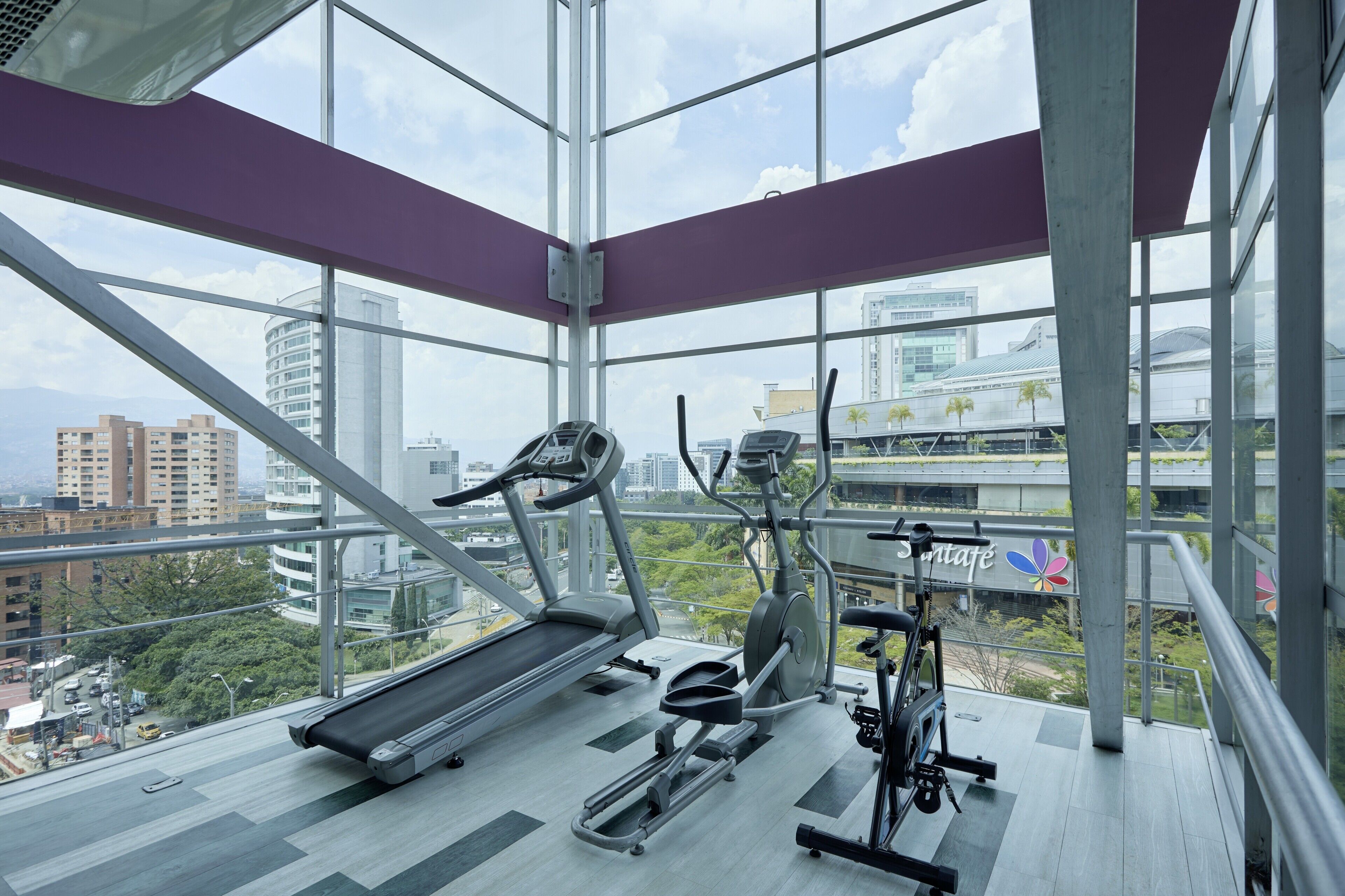 Une salle de sport équipée de matériel d’exercice et dotée de grandes fenêtres offrant une vue sur la ville.