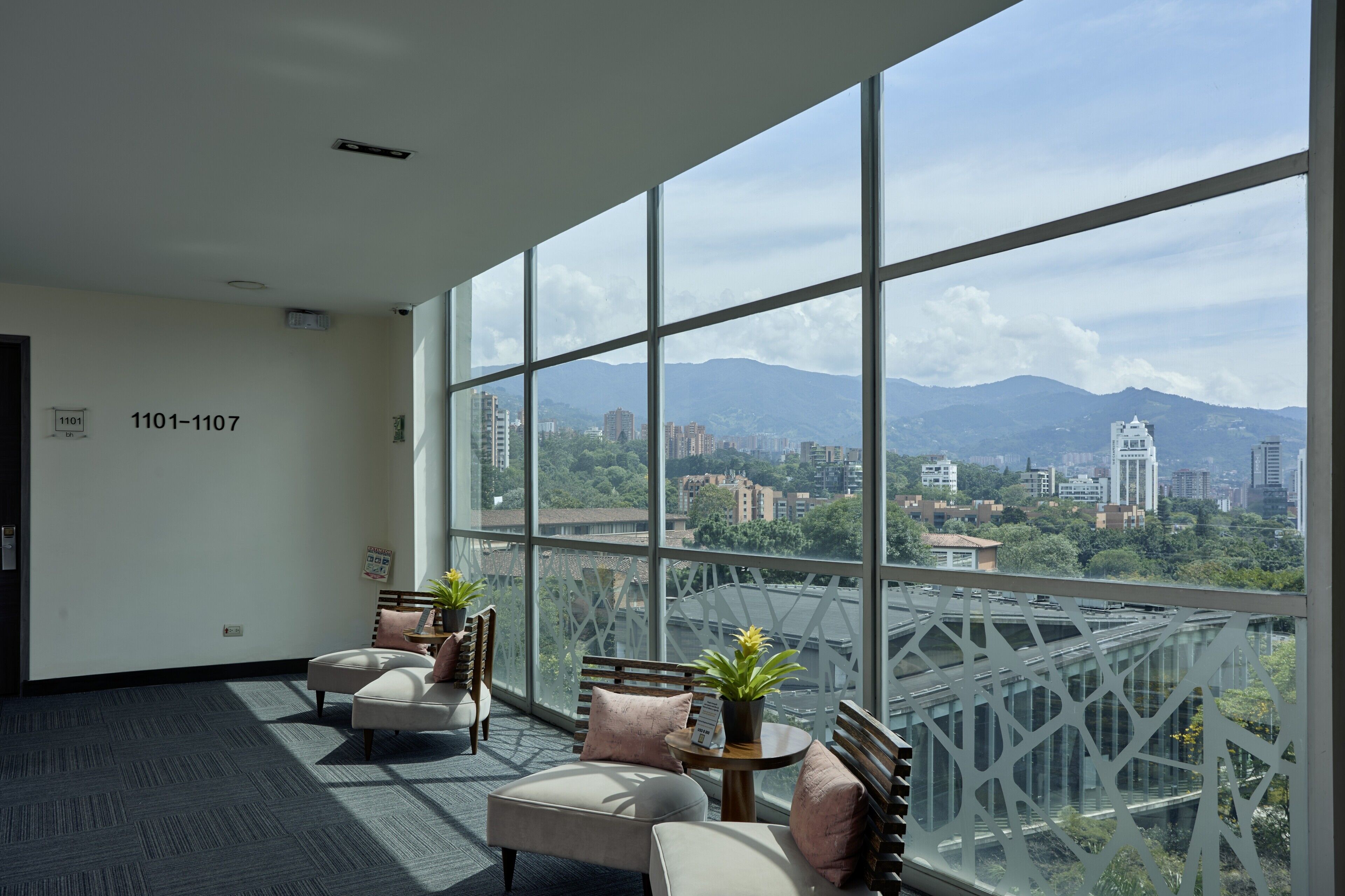 A spacious room with large windows, a sofa, a small table with a plant, and a view of a cityscape with mountains in the distance.