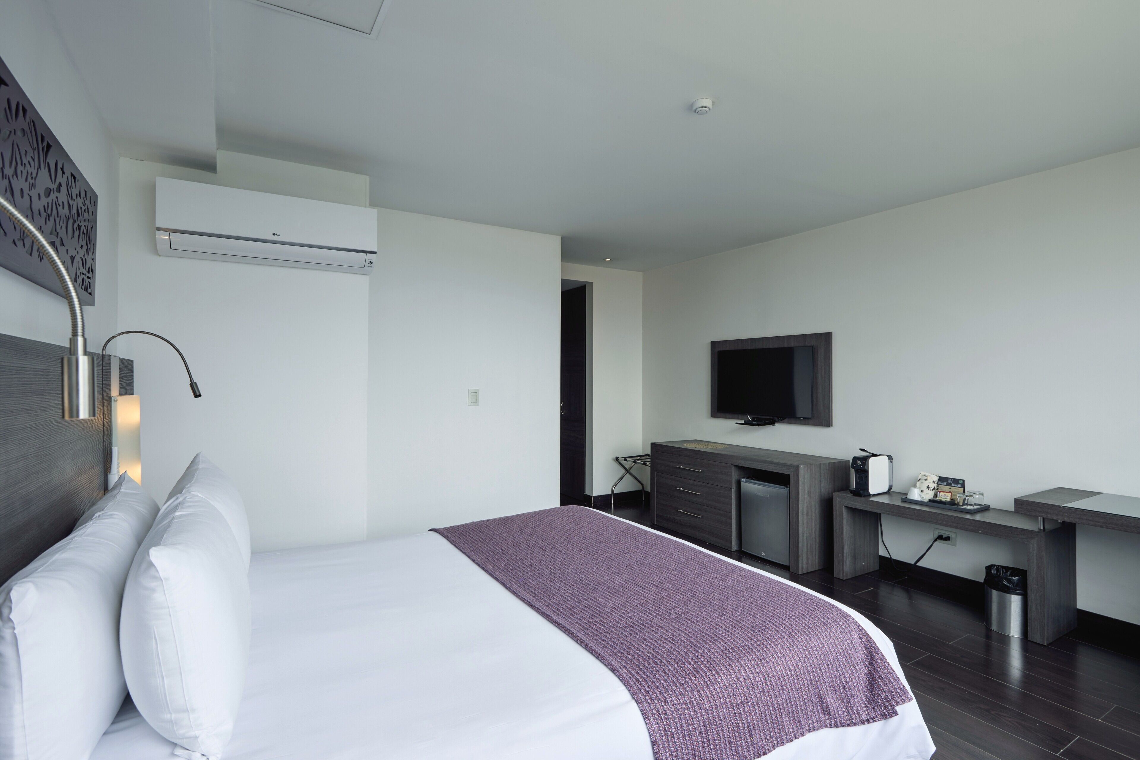 Une chambre d’hôtel moderne équipée d’un lit, d’un bureau, d’une télévision et d’un appareil de climatisation.