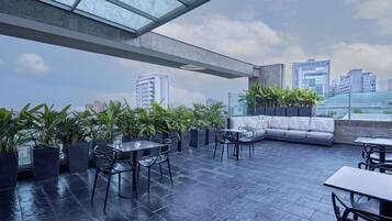 A rooftop terrace with a seating area, tables, and potted plants.