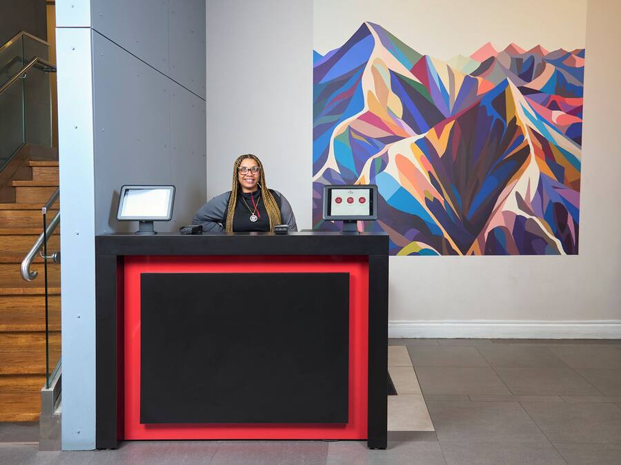 A reception desk with two monitors, a person standing behind it, and a colorful abstract painting on the wall.
