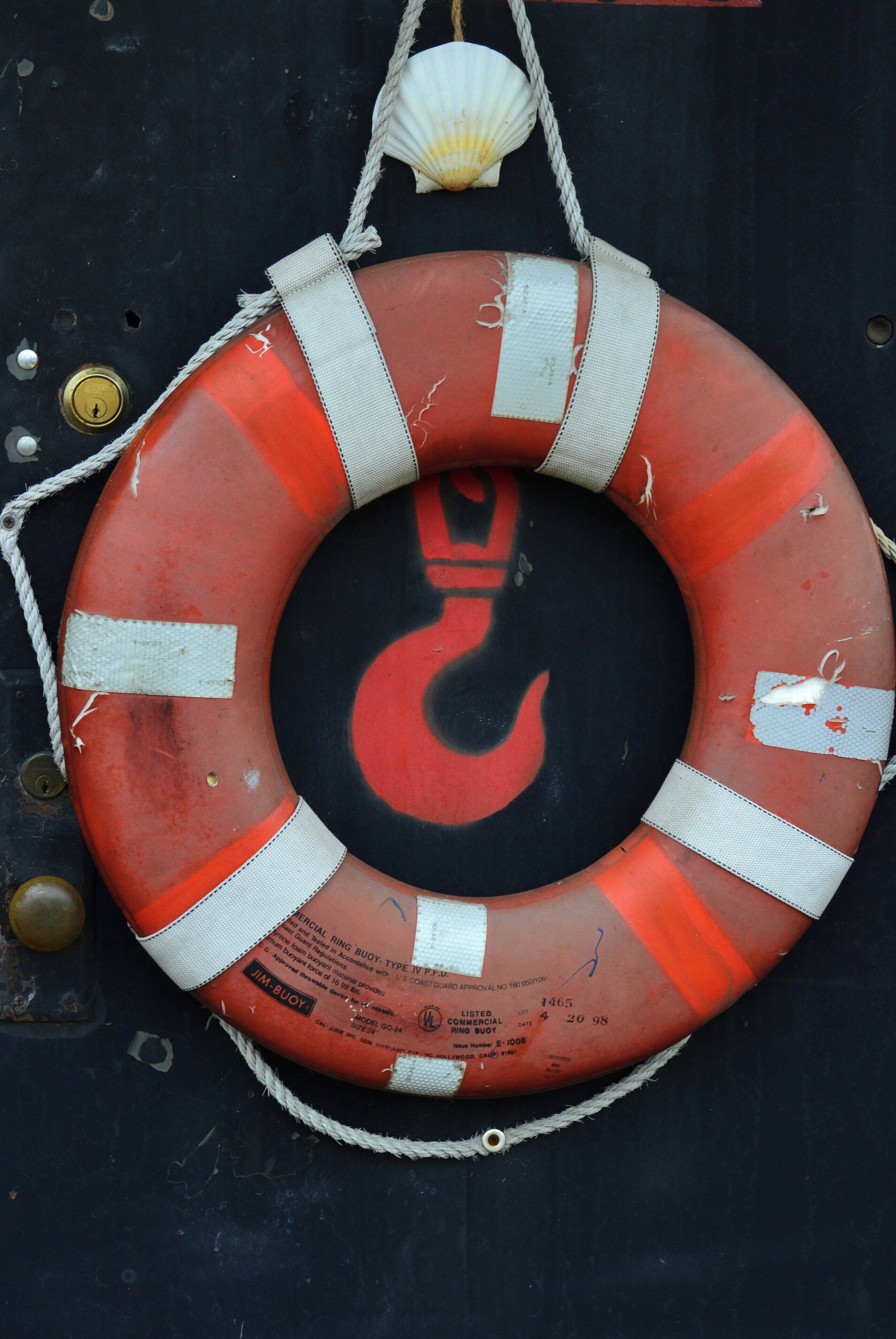 A lifebuoy with a red and white design, attached to a rope, against a dark background.