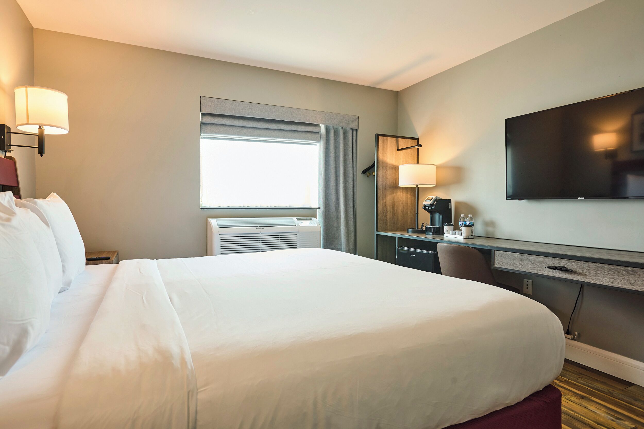 Habitación de hotel con una cama grande, un escritorio con computadora, un televisor de pantalla plana y una ventana con cortinas.