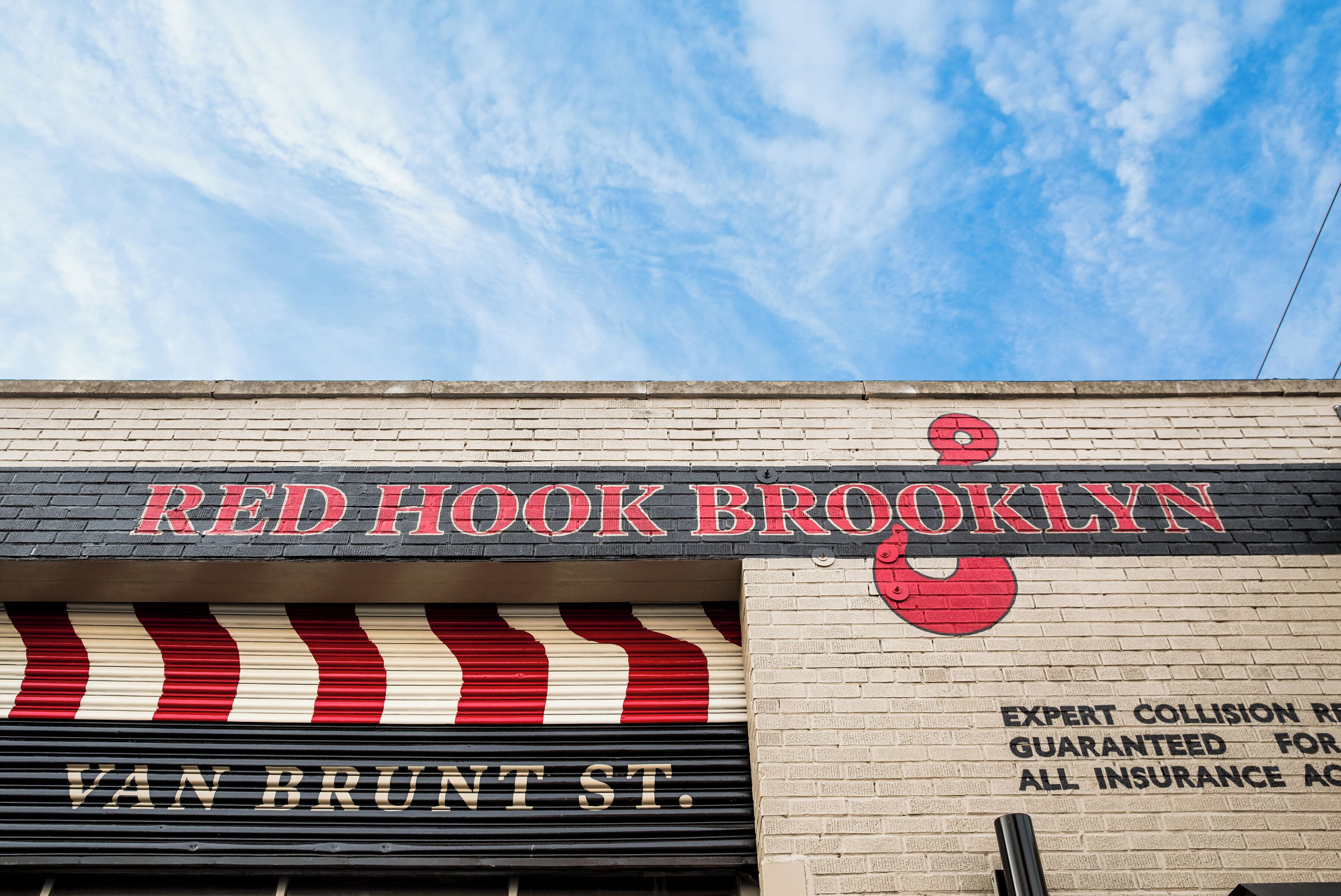 Außenansicht von Red Hook, Brooklyn, mit einem markanten, rot-weiß gestreiften Markisenbalken und blauem Himmel.