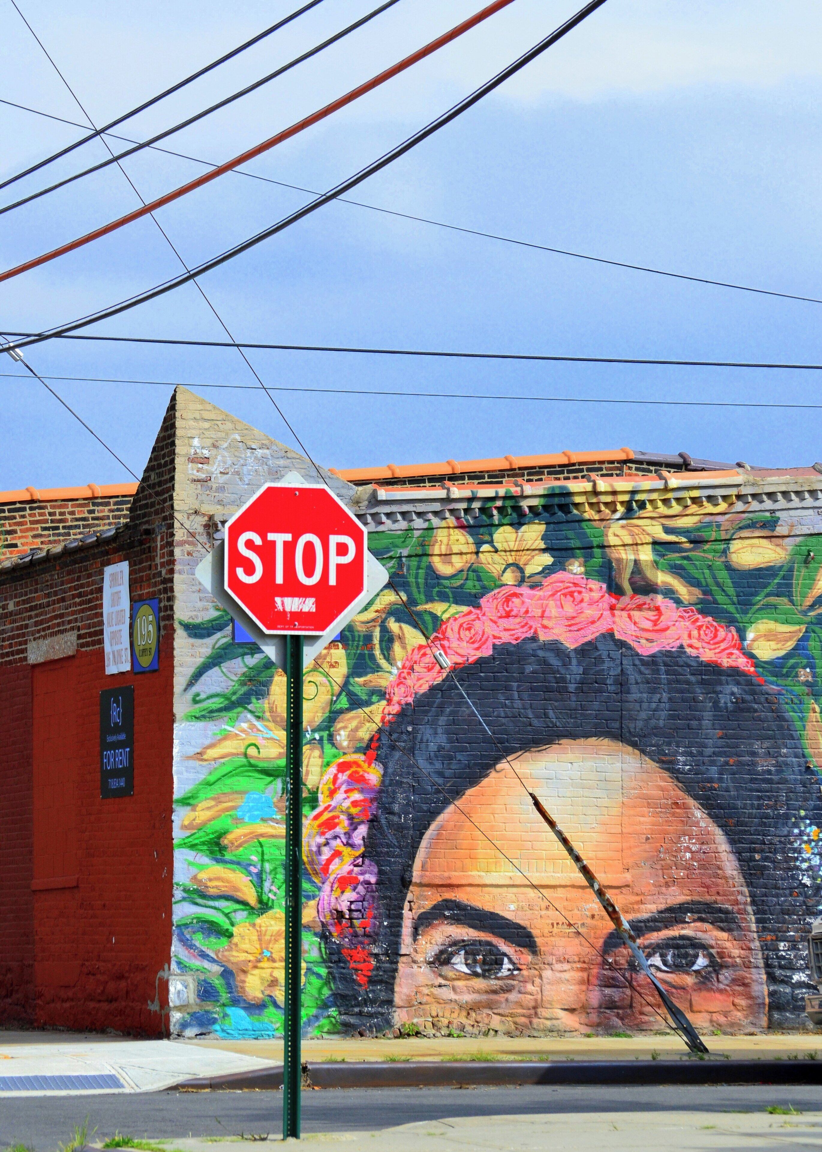 Una señal de alto frente a un mural con el rostro de una mujer.