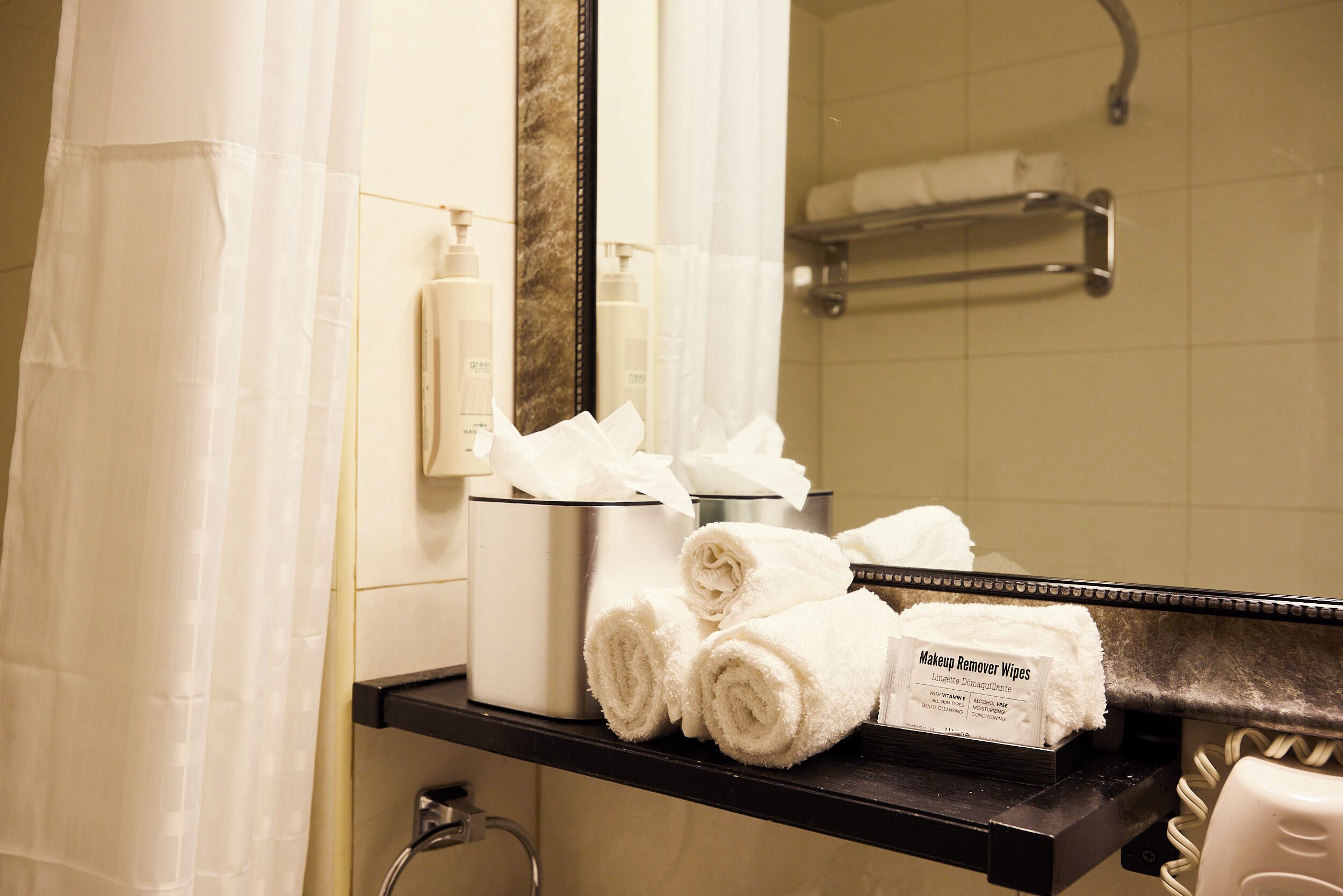 Une salle de bain équipée d’un porte-serviettes où sont rangées des serviettes pliées, d’un distributeur de lingettes démaquillantes et d’un miroir.