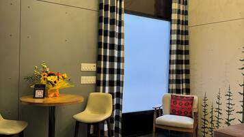 A modern room with a large window, checkered curtains, a chandelier, and a small table with a vase of flowers.