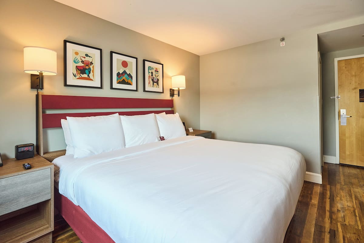 A hotel room with a large bed, two bedside tables, a nightstand, and three framed artworks on the wall.