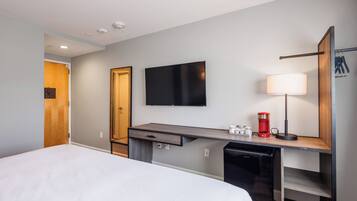 A hotel room with a bed, a desk with a flat-screen TV, a lamp, and a coffee maker.