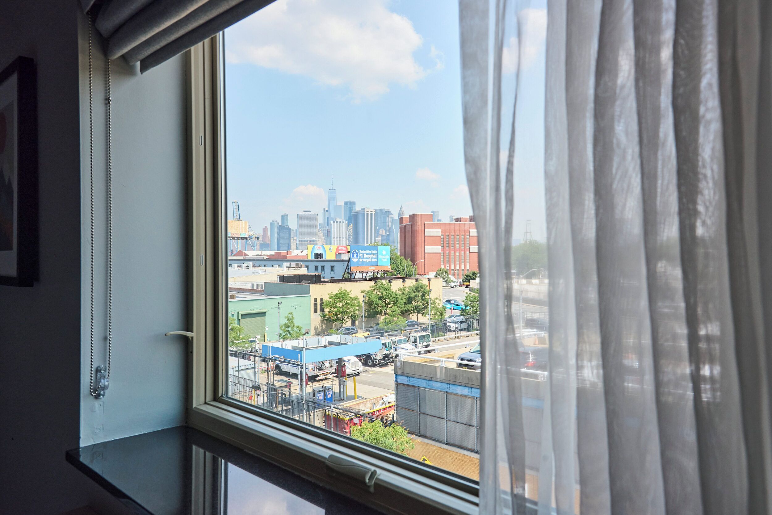 Blick aus einem Fenster mit Vorhängen auf einen Stadtblick mit Gebäuden und einem Parkplatz.