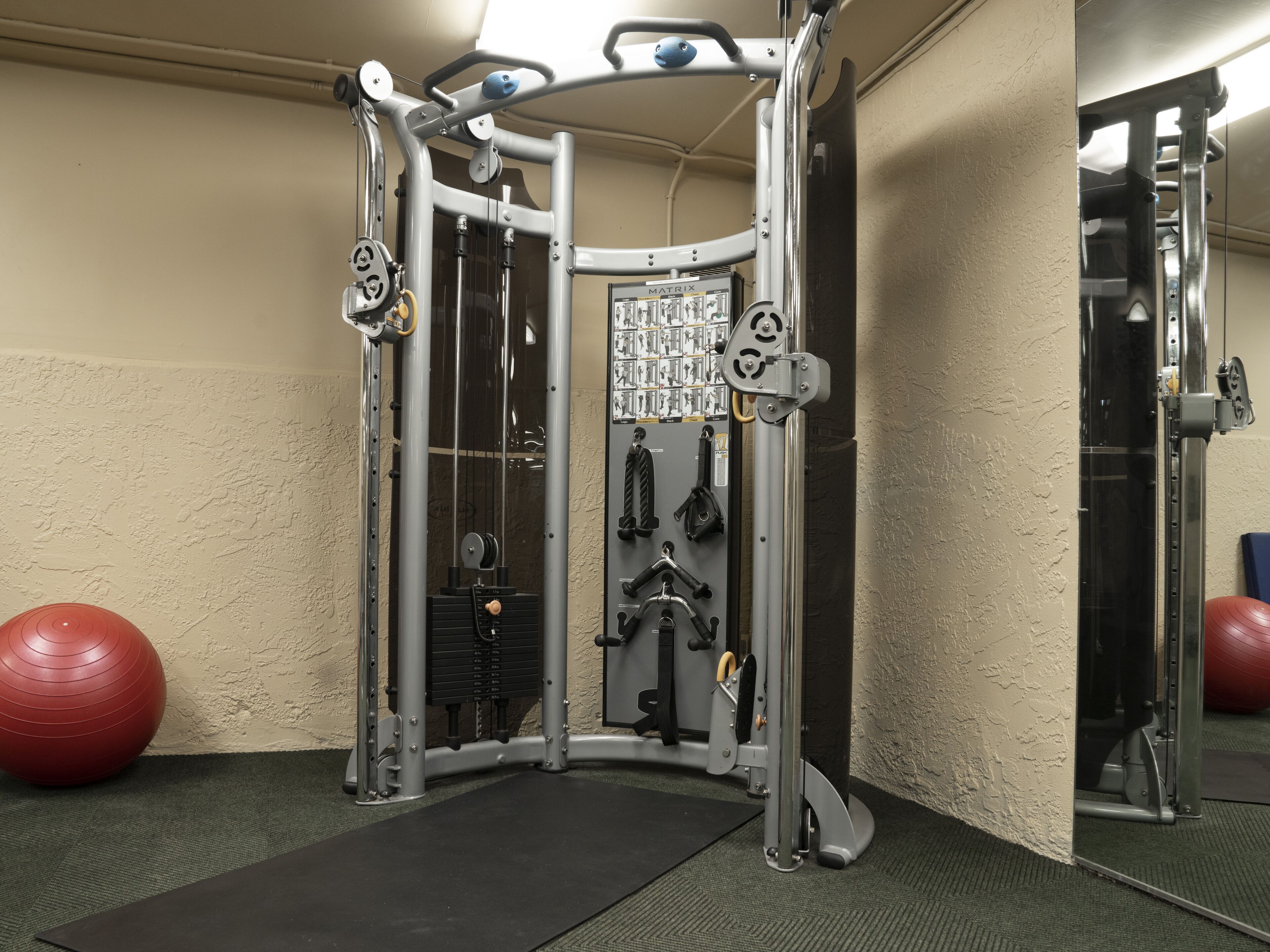 A gym with a cable machine, exercise balls, and a mirror.