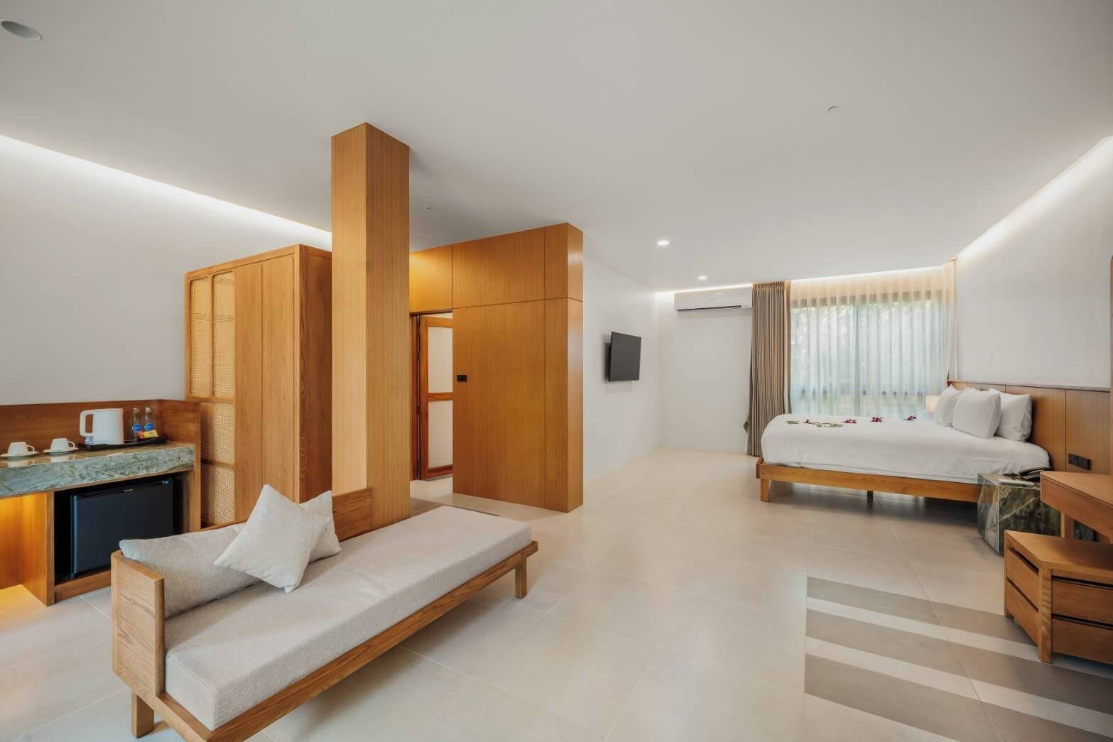 A modern hotel room with a sofa, a bed, a desk, and a small kitchenette.