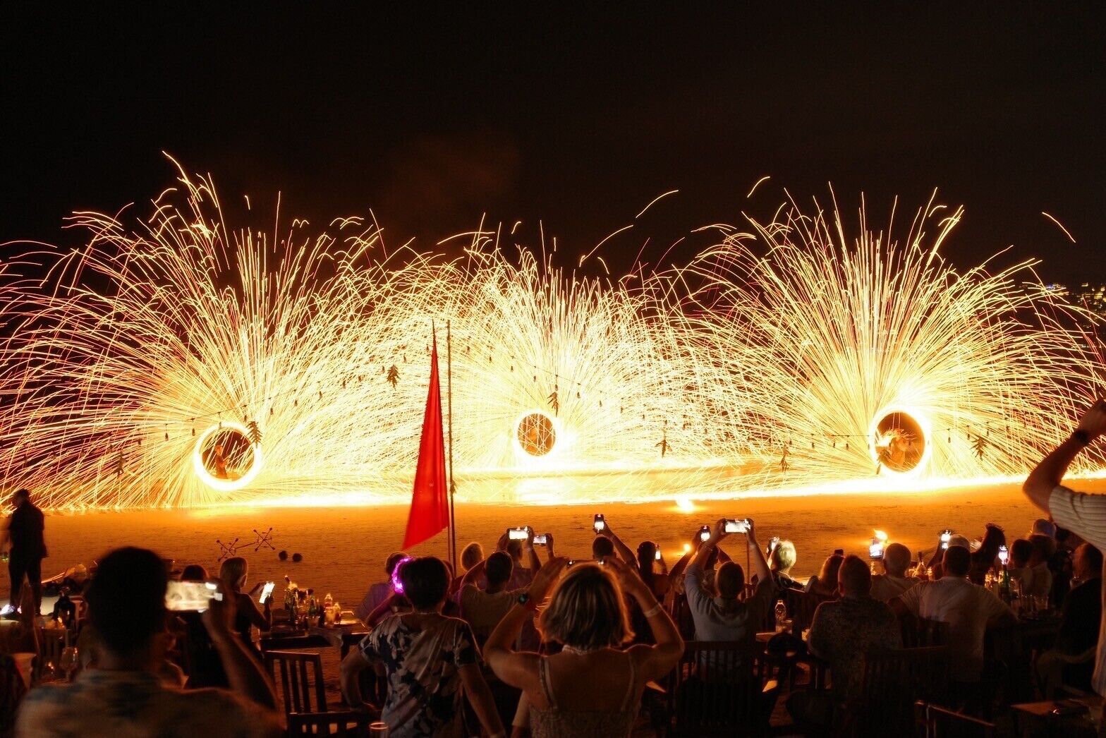 A nighttime outdoor event with firework displays and a crowd of people.