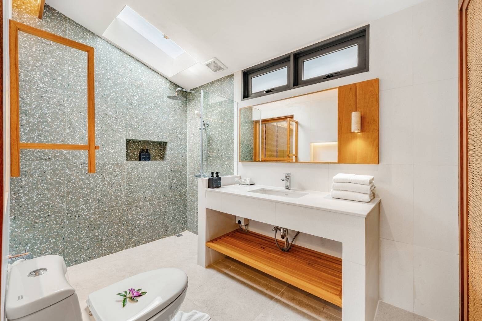 Une salle de bain moderne avec un mur de douche en granit, un grand miroir, un lavabo blanc et des toilettes.