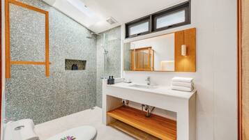 Une salle de bain moderne avec un mur de douche en granit, un grand miroir, un lavabo blanc et des toilettes.