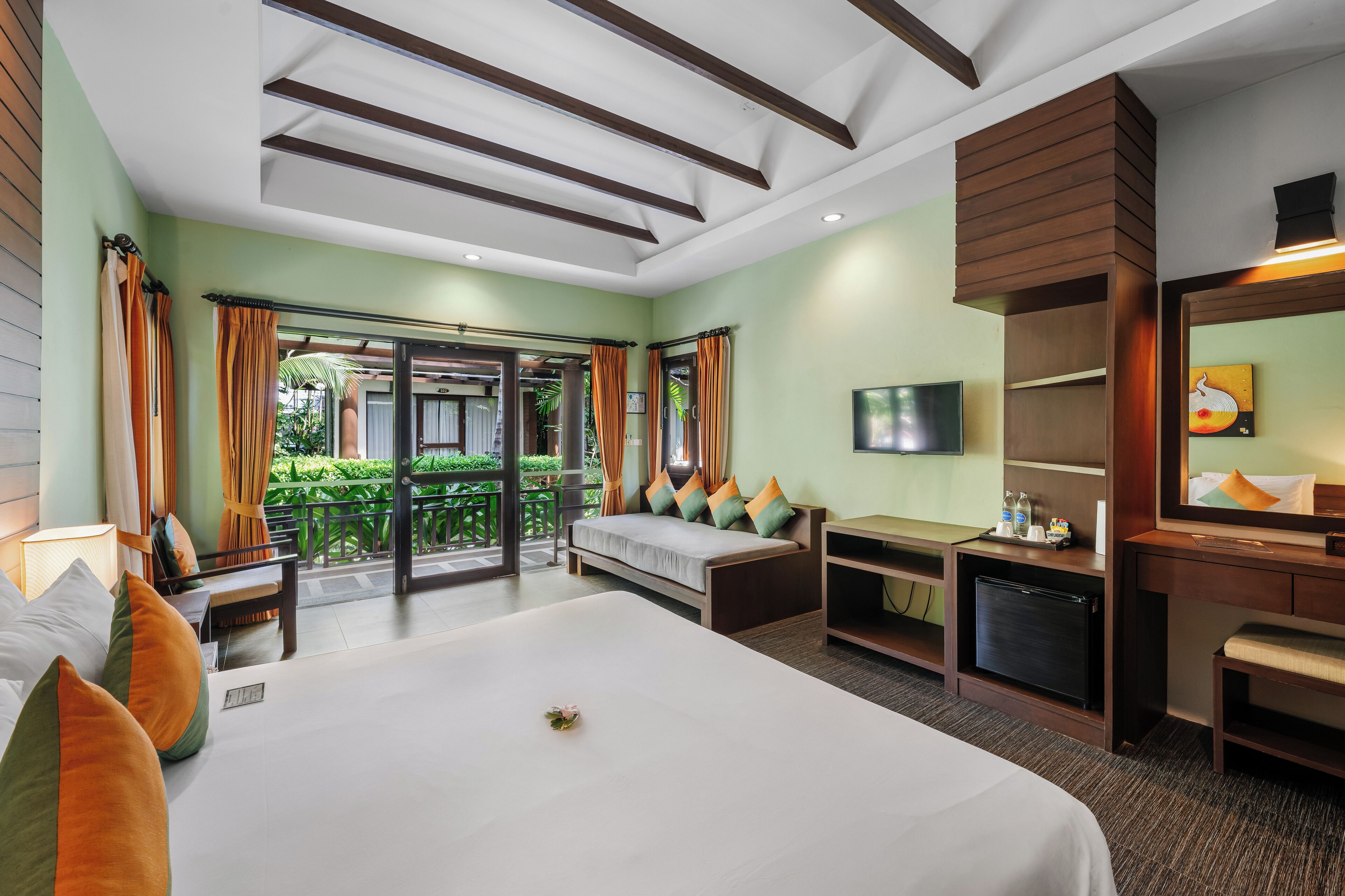 A hotel room with a large bed, a sofa, a desk with a TV, and a balcony with curtains.
