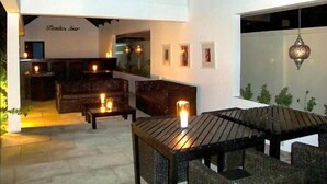 An outdoor seating area with wooden furniture and candles, a bar area with a sign reading "Tindes Bar", and a hanging lantern. - The Aknac Hotel (Accra)