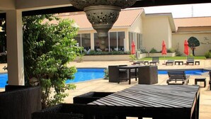 An outdoor patio area with a pool, wicker furniture, and a decorative metal lamp. - The Aknac Hotel (Accra)