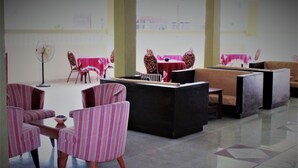 A hotel lobby with striped armchairs, a fan, and tables with red tablecloths. - Badala Park Hotel (Serrekunda)