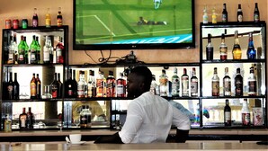 A bar with a television displaying a sports event, shelves stocked with various liquor bottles, and a bar counter with a cup and saucer. - Badala Park Hotel (Serrekunda)