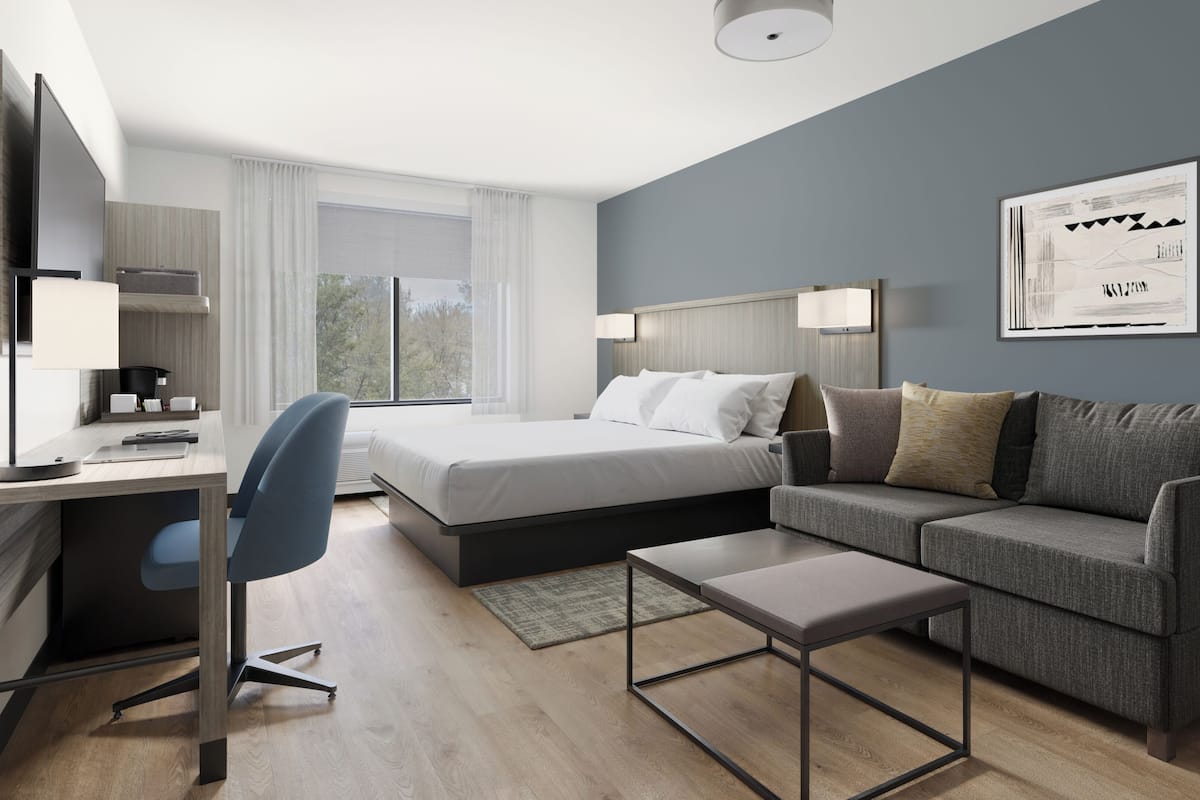 Ett modernt hotellrum med en säng, ett skrivbord, en stol, en soffa och en inramad tavla på väggen.
