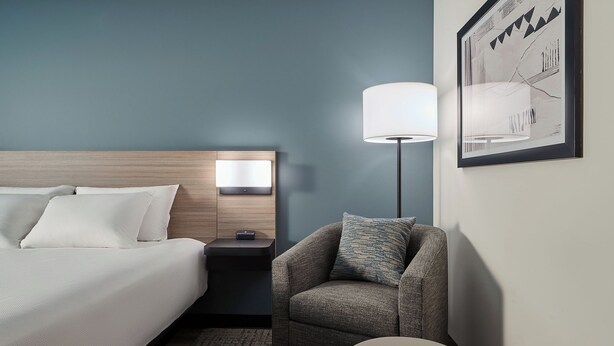 A hotel room with a bed, a nightstand, a lamp, a chair, and a rug. - Hyatt Select Philadelphia Airport (Essington)