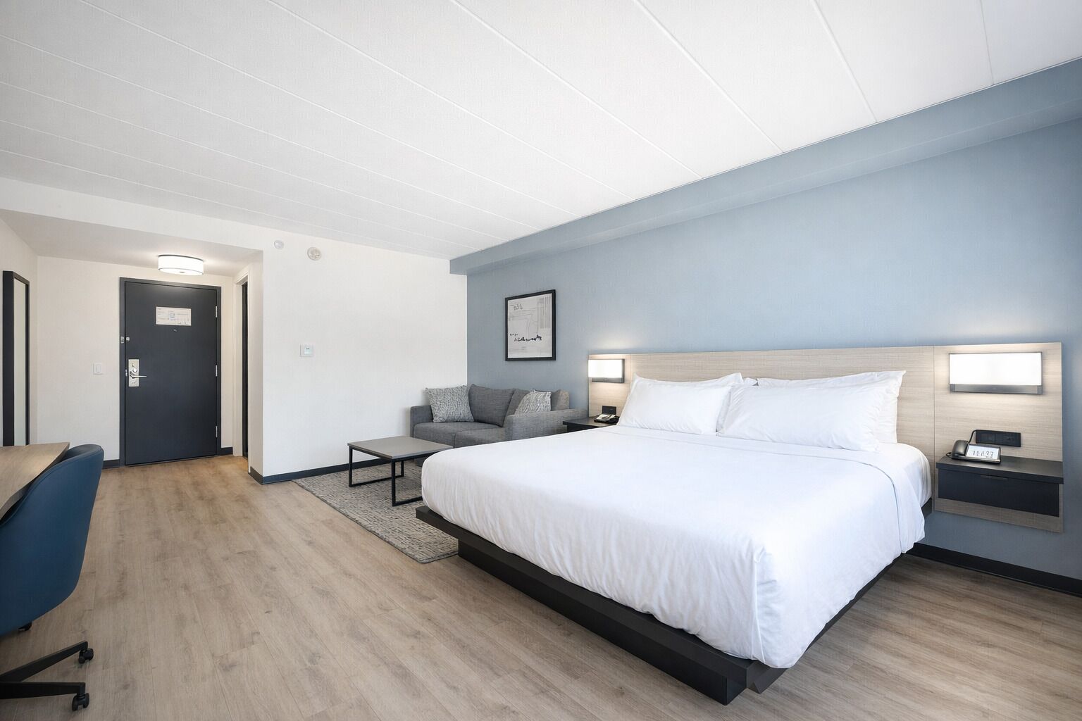 A modern hotel room with a large bed, bedside tables, a desk, and a sofa.