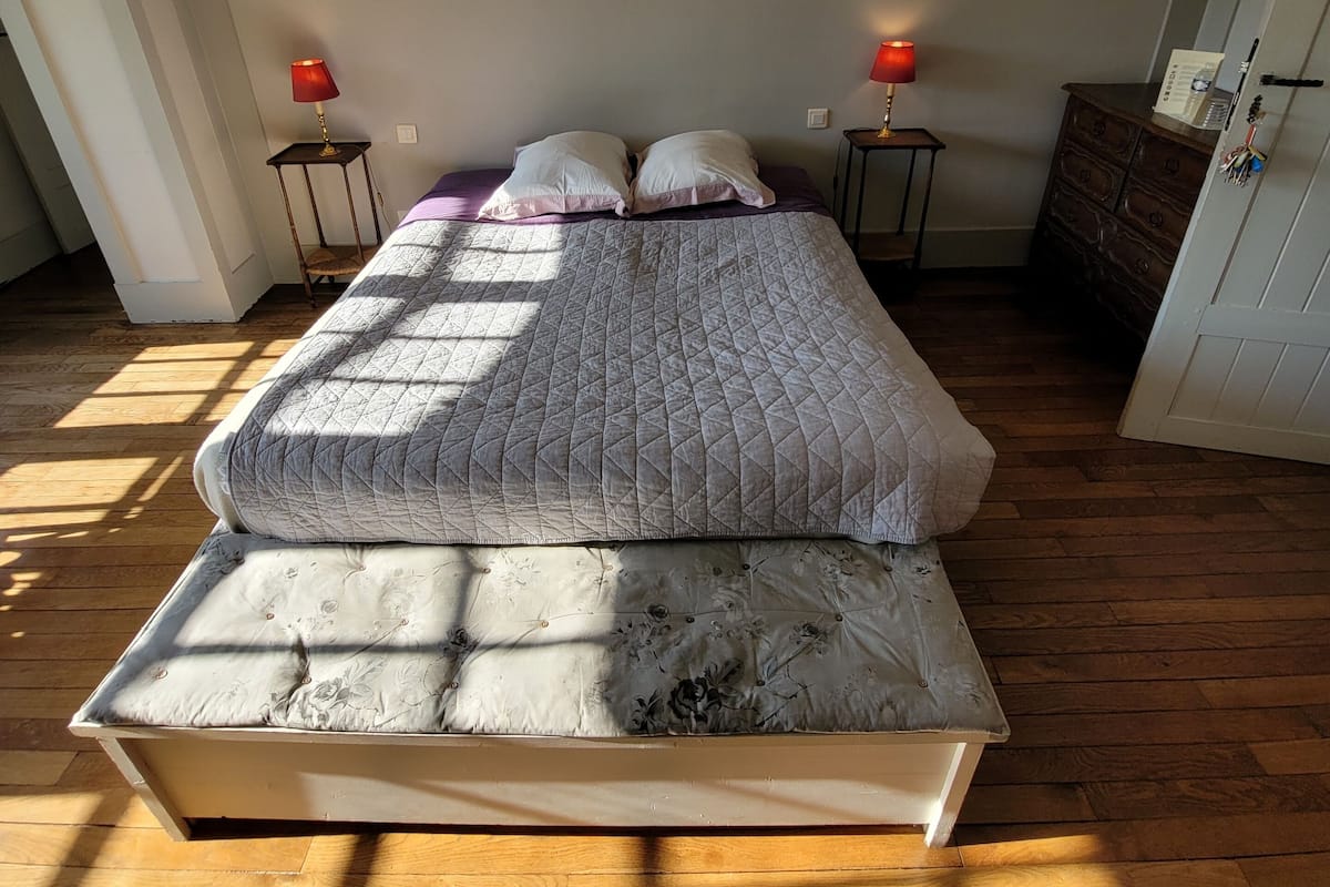 Un lit recouvert d’une courtepointe, deux tables de chevet avec des lampes, une commode et un miroir au mur.