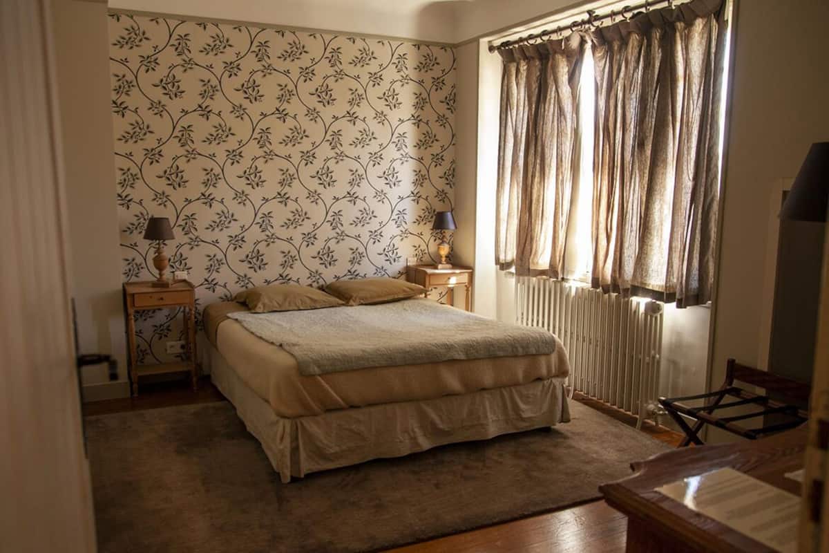 Une chambre à coucher avec un lit, deux tables de chevet avec des lampes, un radiateur et une fenêtre avec des rideaux.