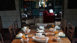 A dining table set with breakfast items including pastries, bread, and beverages, in a room with wooden furniture and a hanging light fixture. - Chambres d'Hôtes Le Manoir de Beaumarchais (Les Chapelles-Bourbon)