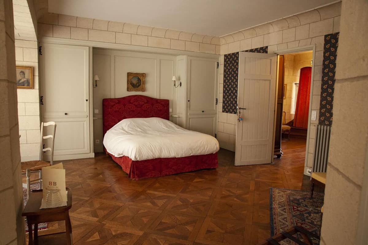 Une chambre avec un grand lit, un plancher en bois et une porte donnant sur une autre pièce.