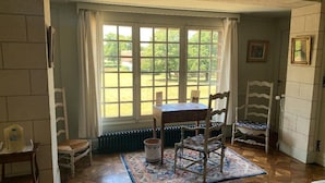 A room with a table and chairs near a window, a radiator, and a door with a picture on the wall. - Chambres d'Hôtes Le Manoir de Beaumarchais (Les Chapelles-Bourbon)