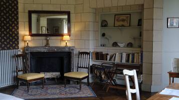 A room with a fireplace, two chairs, a bookshelf, and a mirror.