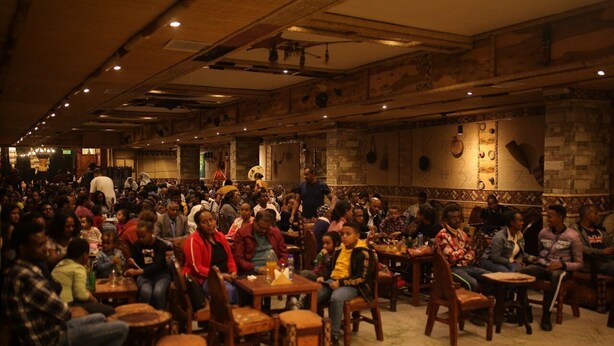 A crowded indoor space with wooden tables and chairs, stone walls, and a high ceiling. - Soramba Hotel (Addis Ababa)