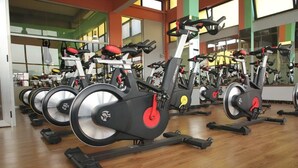 A row of stationary bikes in a gym with mirrored walls and large windows. - Soramba Hotel (Addis Ababa)