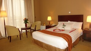 A hotel room with a large bed, two bedside tables, a chair, a desk, and a lamp. - Soramba Hotel (Addis Ababa)