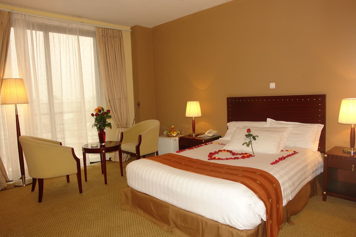 Una habitación de hotel con una cama grande, dos mesitas de noche, una silla, un escritorio y una lámpara.