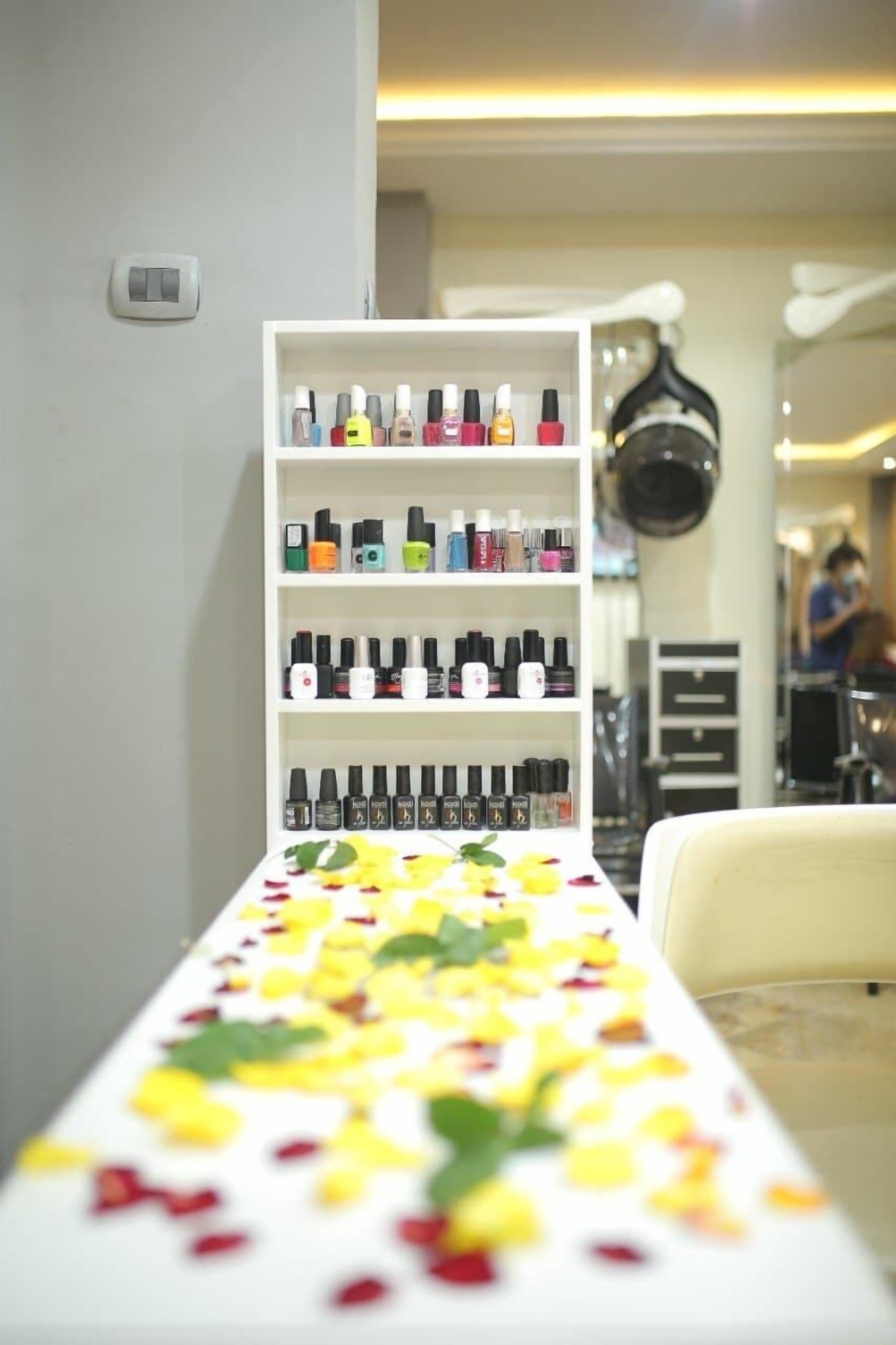 Un salón con una estantería blanca llena de frascos de esmalte de uñas de diferentes colores.