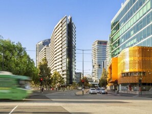 A modern urban street with tall buildings, a green bus, and cars. - Docklands Executive Apartments (Docklands)