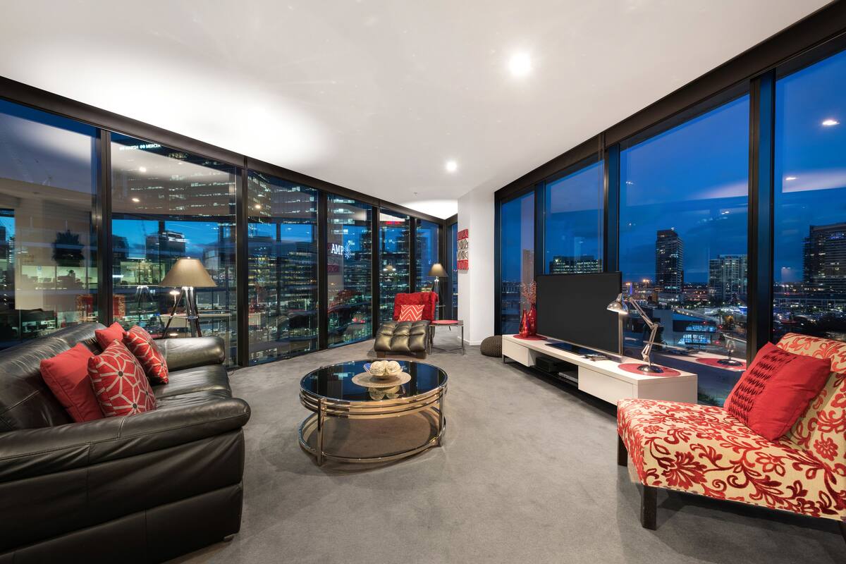 A modern living room with a city view, a leather sofa, a patterned armchair, and a glass coffee table.