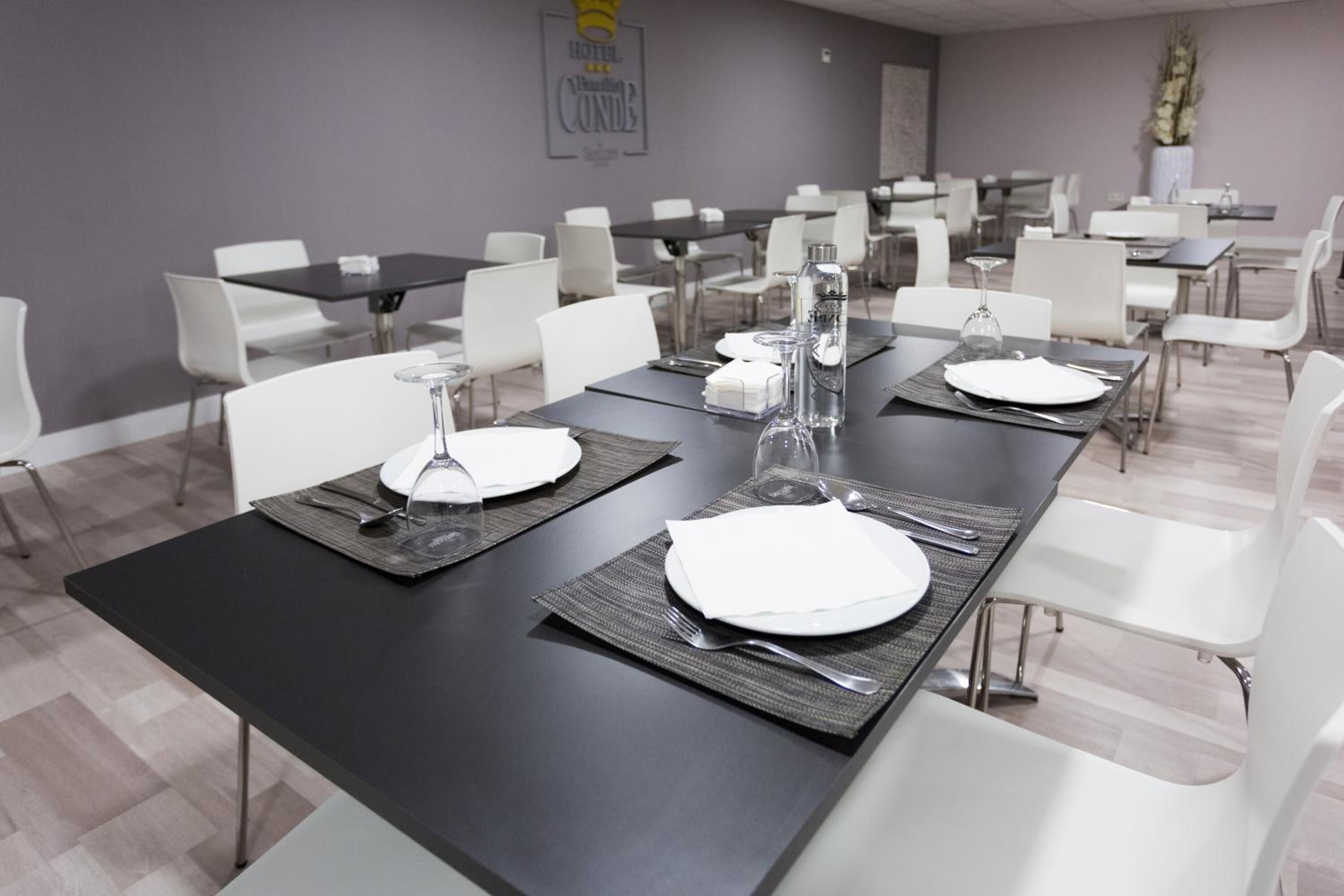 A hotel dining area with tables set for four, each with a white plate, cutlery, and a glass.