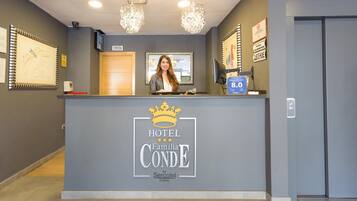 Bancada de recepção do Hotel Familia Conde com logotipo de coroa, uma tela digital e placa indicando disponibilidade de quartos.