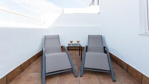 A rooftop terrace with two lounge chairs and a small table with two drinks.