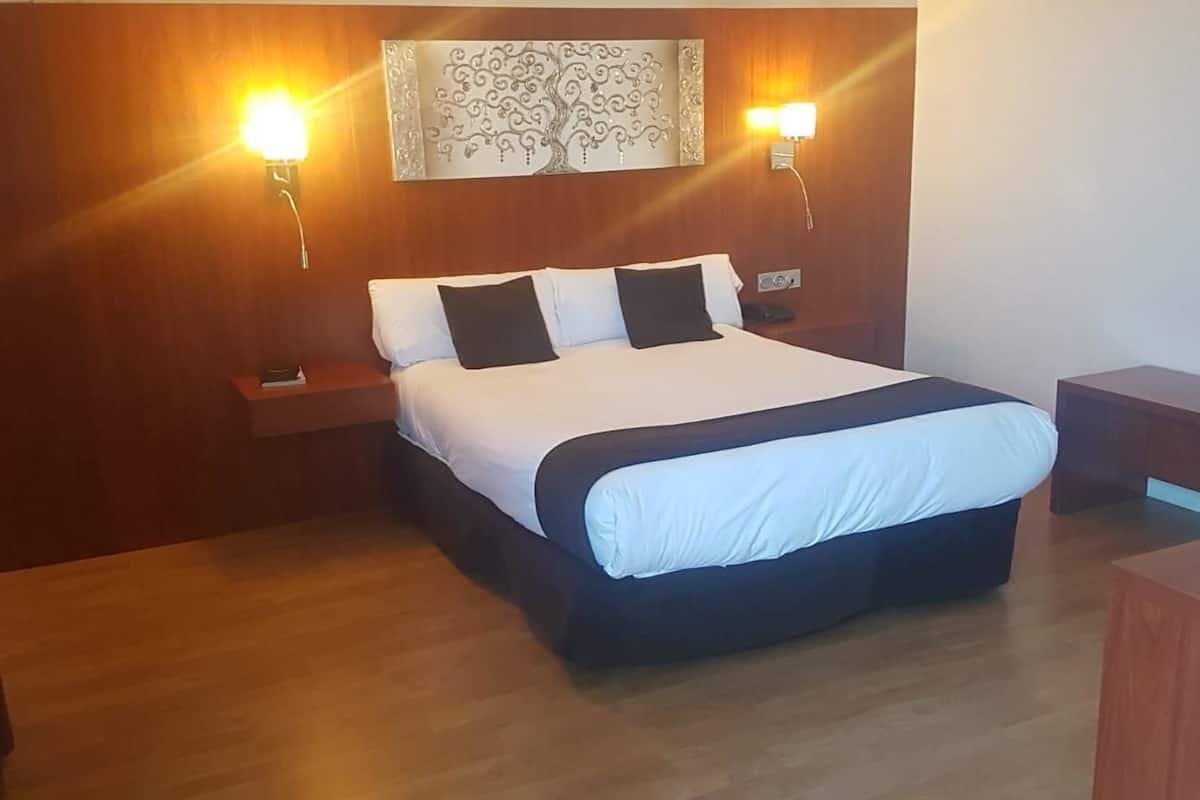 Un dormitorio ordenado con una cama grande, dos mesitas de noche y una lámpara de pared.